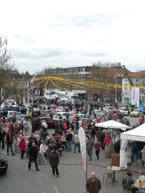 Bild vergr&ouml;&szlig;ern: Gro&szlig;e Menschenmenge auf einem Platz mit zahlreichen geparkten Autos und gelben Girlanden &uuml;ber der Stra&szlig;e bei der Neust&auml;dter Automeile 2012