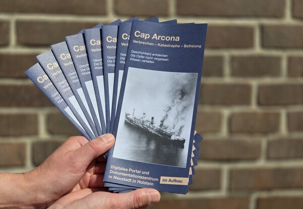 Bild vergr&ouml;&szlig;ern: Eine Hand h�lt Flyer vom Cap-Arcona-Dokumentationszentrum