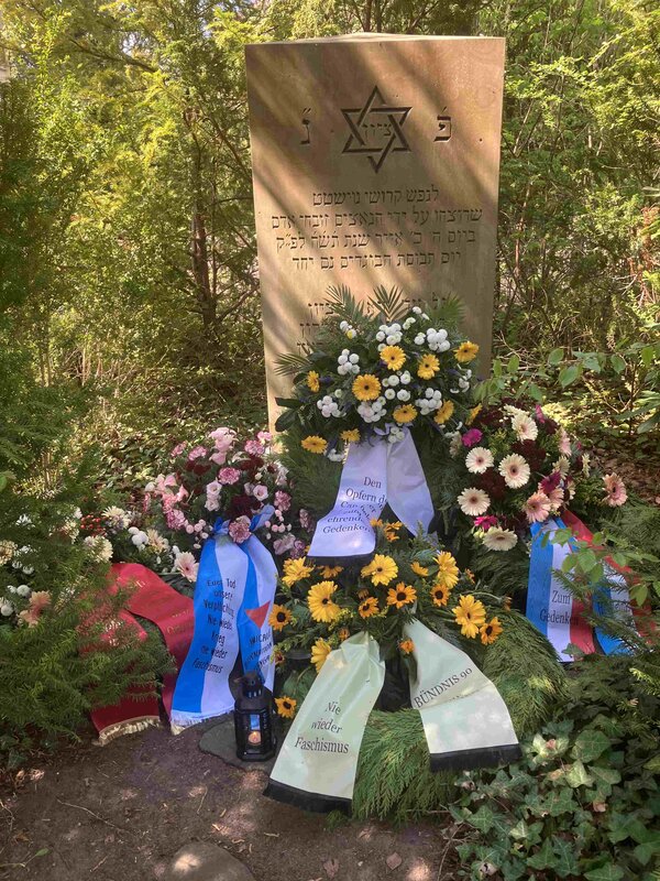 Bild vergr&ouml;&szlig;ern: Grabstein mit Davidstern und hebr&auml;ischer Inschrift auf dem j&uuml;dischen Friedhof in Neustadt in Holstein umgeben von mehreren Kr&auml;nzen mit Schleifen