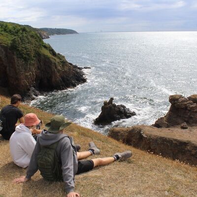 Bild vergr&ouml;&szlig;ern: Eine kleine Gruppe Jugendlicher sitzen auf dem Rasen an einer Klippe am Meer